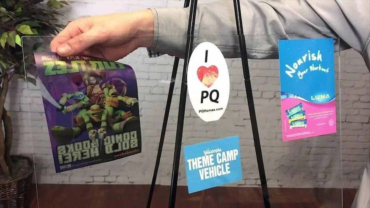 Hand holding a display board with various static cling vinyl stickers including cartoon, heart, and informational designs.