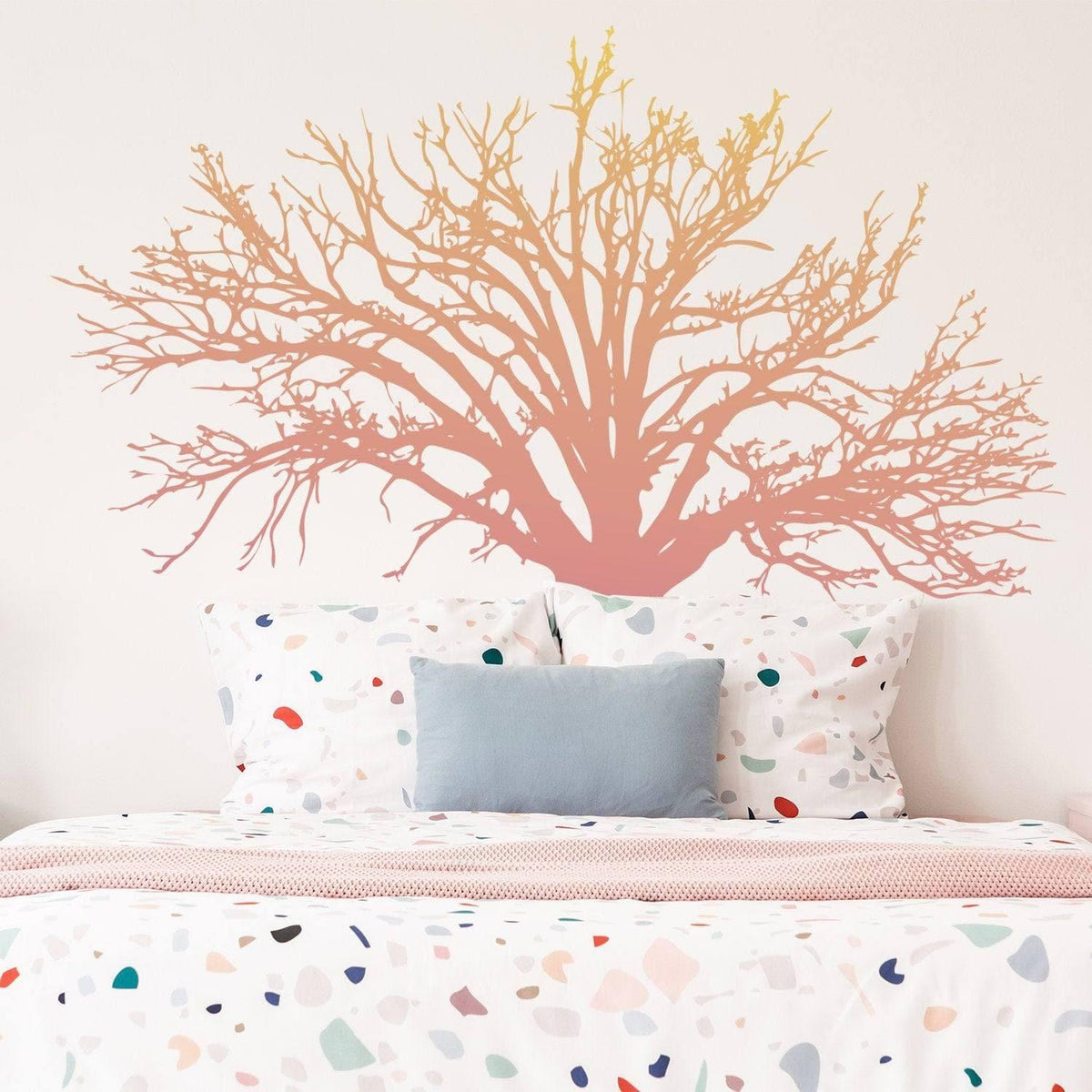 Artistic tree wall decal in soft colors applied above a bed with patterned bedding, enhancing room decor.