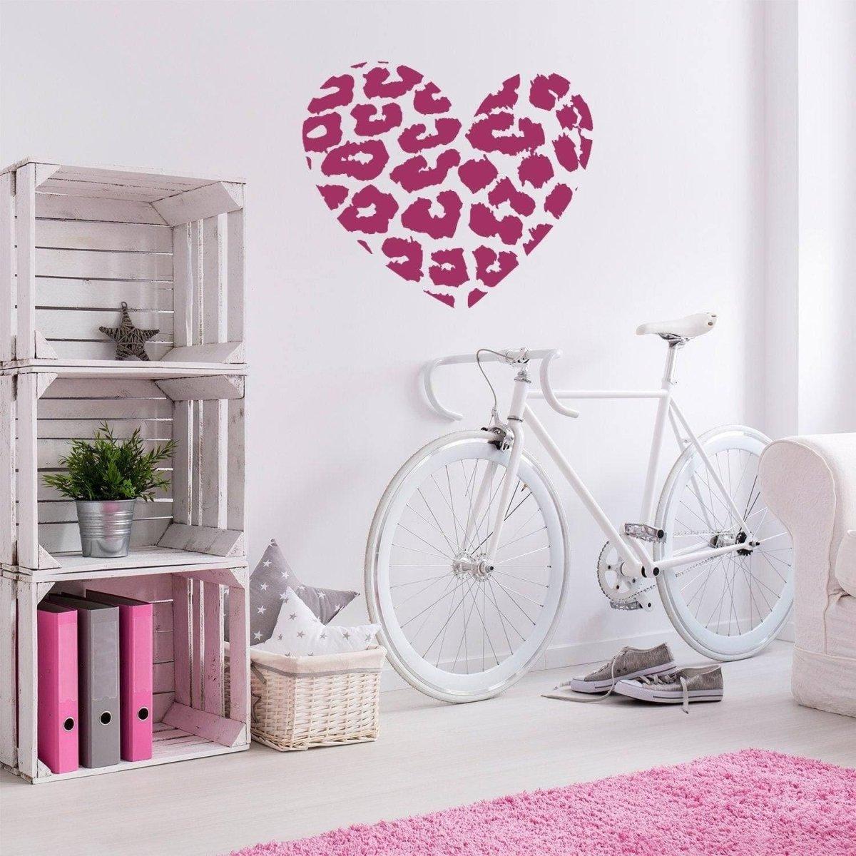 Leopard heart vinyl wall art decal in pink on a white wall, enhancing a modern interior space with bicycle decor.