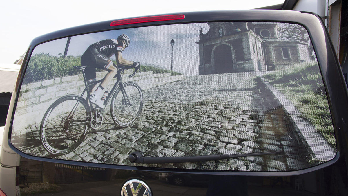 Bicycle rear window decal featuring a cyclist climbing a cobblestone hill near an old building.