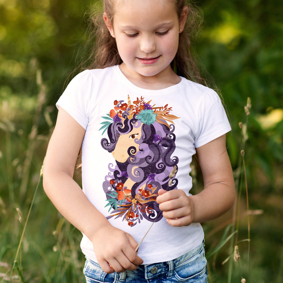 Girl wearing a white t-shirt with a colorful floral design, standing in a field, smiling.