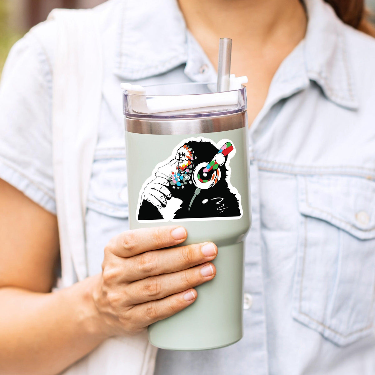 Person holding a mint green tumbler with a colorful monkey design sticker.