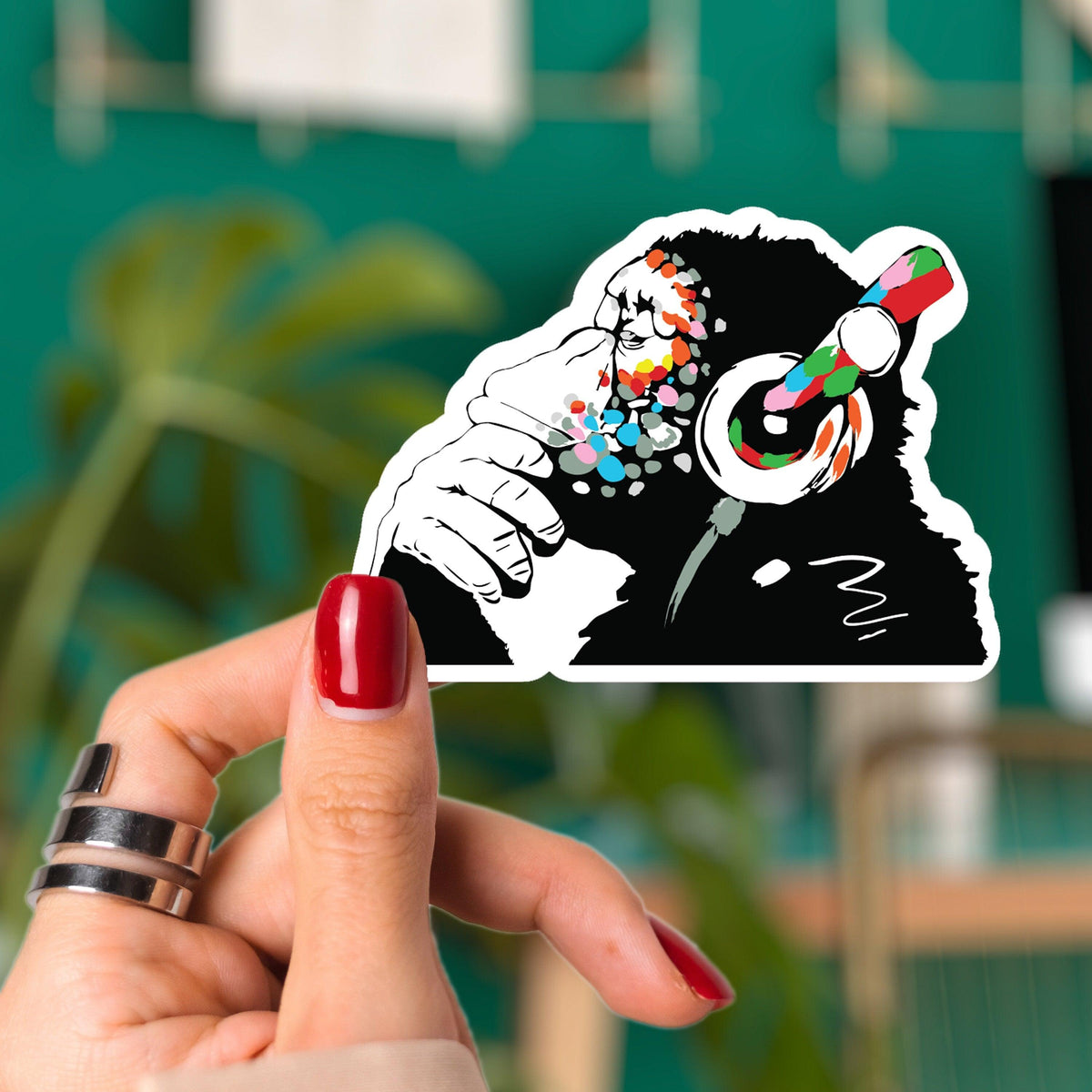 Glow in the Dark Monkey Laptop Vinyl Sticker held by a hand, showcasing the colorful monkey with headphones design.