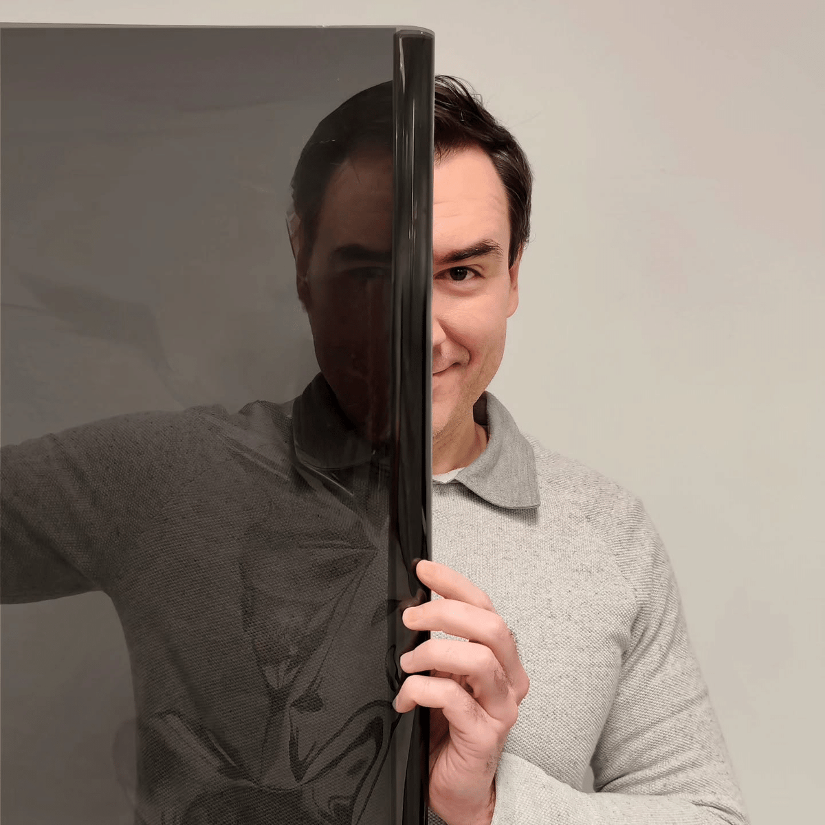A man holding a roll of dark window film, with part of his face visible through the film.