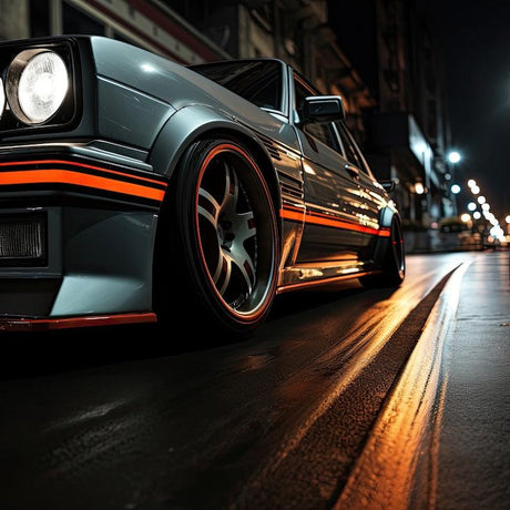 Close-up of a stylish car with orange geometric peel-and-stick decals parked on a city street at night.