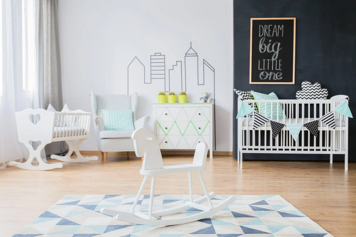 Stylish nursery with chalkboard wall, white furniture, and playful decor featuring rockers and bunting.