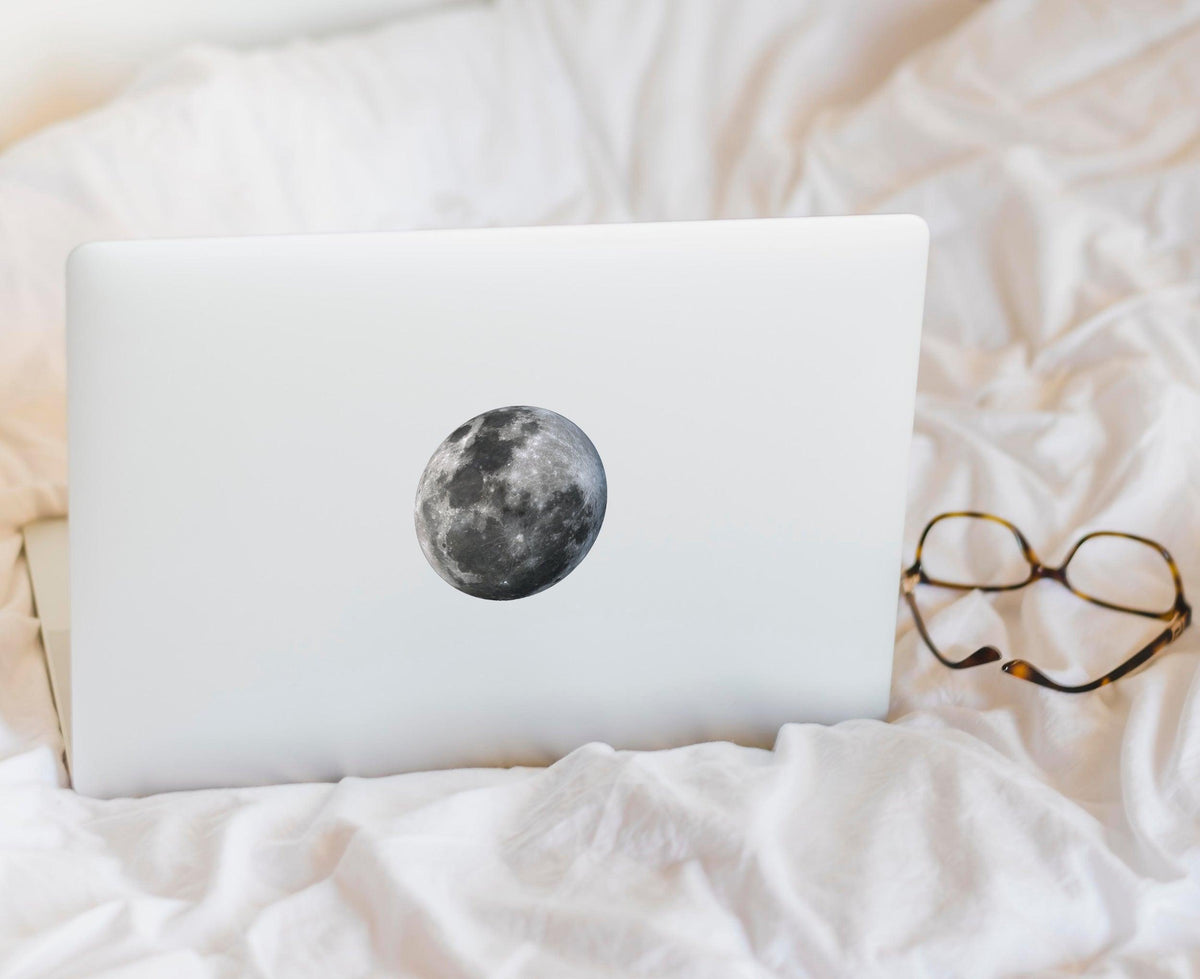 Lunar Luminescence laptop decal featuring a glowing moon on a white laptop resting on soft bedding.