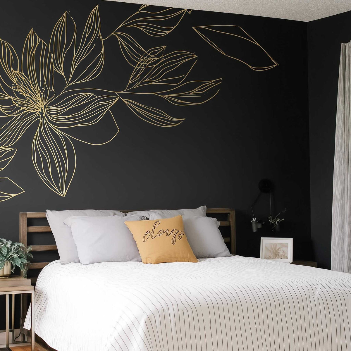 Gold flower wall decal on dark wall above a modern bed with decorative pillows, adding elegance to the bedroom decor.