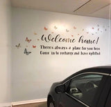 Welcome home lettering and butterfly wall sticker on a light garage wall above a dark parked car.