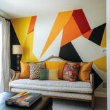 Vibrant geometric wall decal in yellow, orange, black, and red above a cozy sofa in a modern living room.