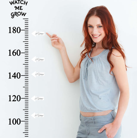 Smiling woman measuring height against a vinyl growth chart ruler decal, showcasing growth milestones.