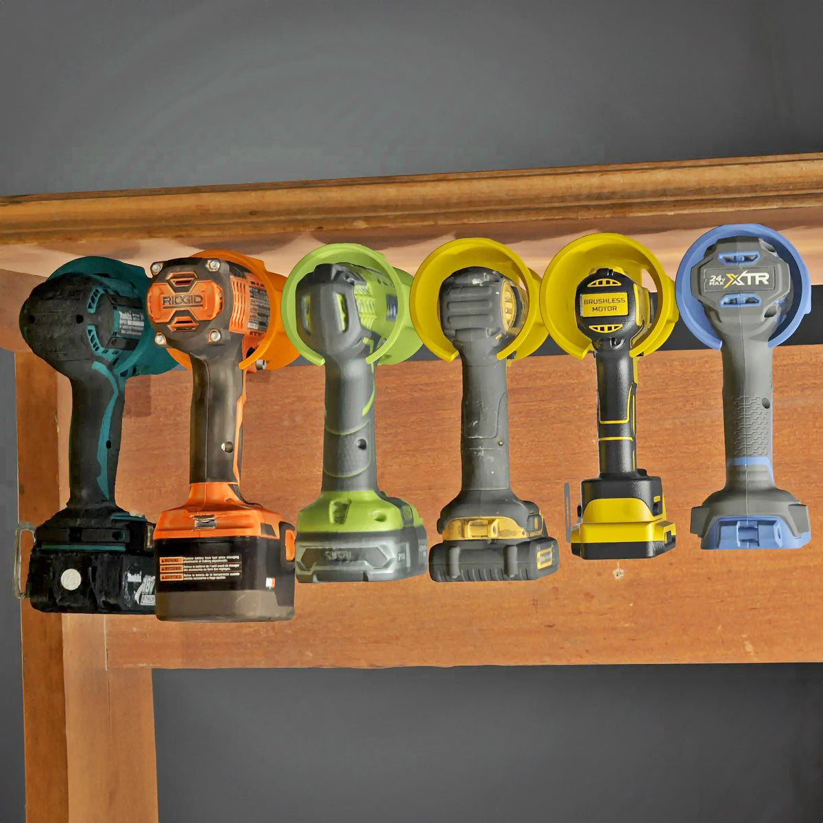 Universal cordless drill holder displaying various drill models mounted under a shelf for organized tool storage.