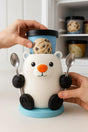 A 3D printed polar bear ice cream holder with a bright orange nose, holding two metal spoons in its paws.