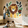 A cute, smiling cartoon lion with a brown mane sitting in front of a decorative wreath of dark green and light green.
