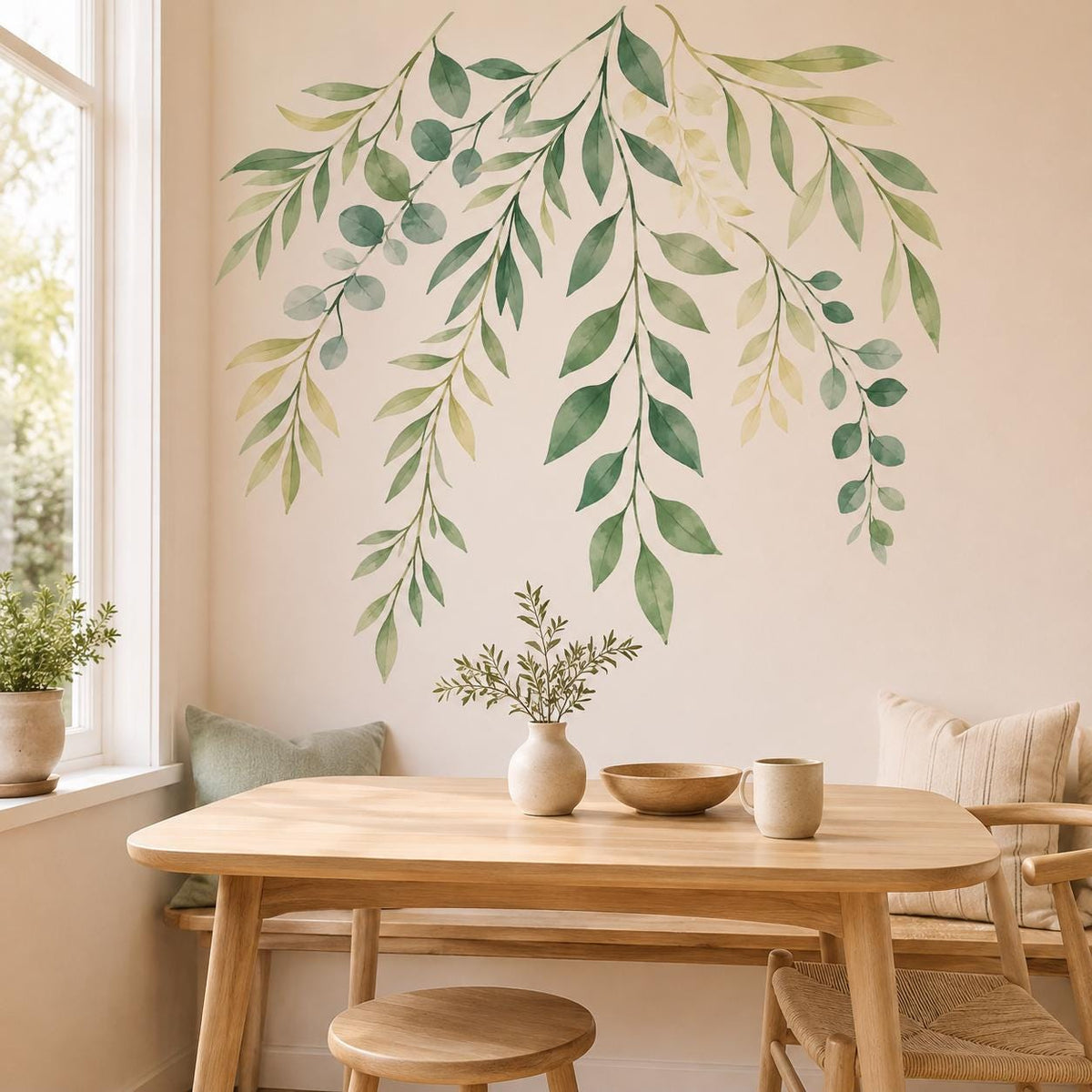 Cascading watercolor sage leaf wall decal above a light wood dining table beside a sunlit window.