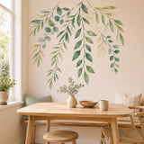 Cascading watercolor sage leaf wall decal above a light wood dining table beside a sunlit window.