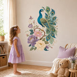 Little girl in a lilac dress looking up at a teal peacock and flower wall decal in a nursery.
