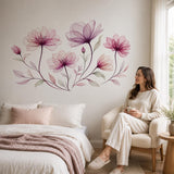 Woman sitting beside a bed beneath a pink flower wall decal in a softly lit bedroom.