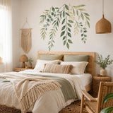 Sage green hanging leafy branches wall decal above a beige bed with woven bedding.