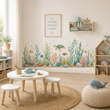 Watercolor sea turtle, fish and coral wall decals above a small table and woven rug in a bright playroom.