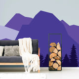 Majestic mountain wall decal in purple tones enhancing a cozy living room with a gray sofa and wood logs.