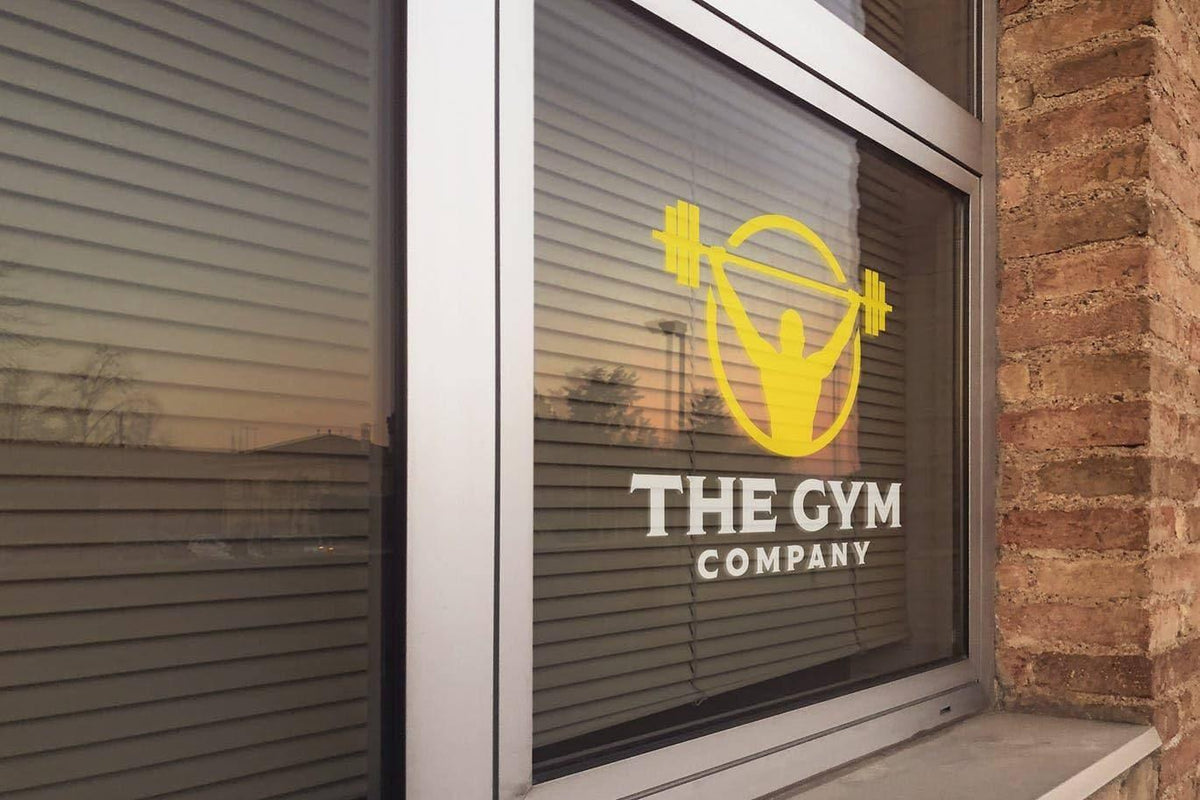 Custom vinyl sticker on gym window displaying logo and weights.
