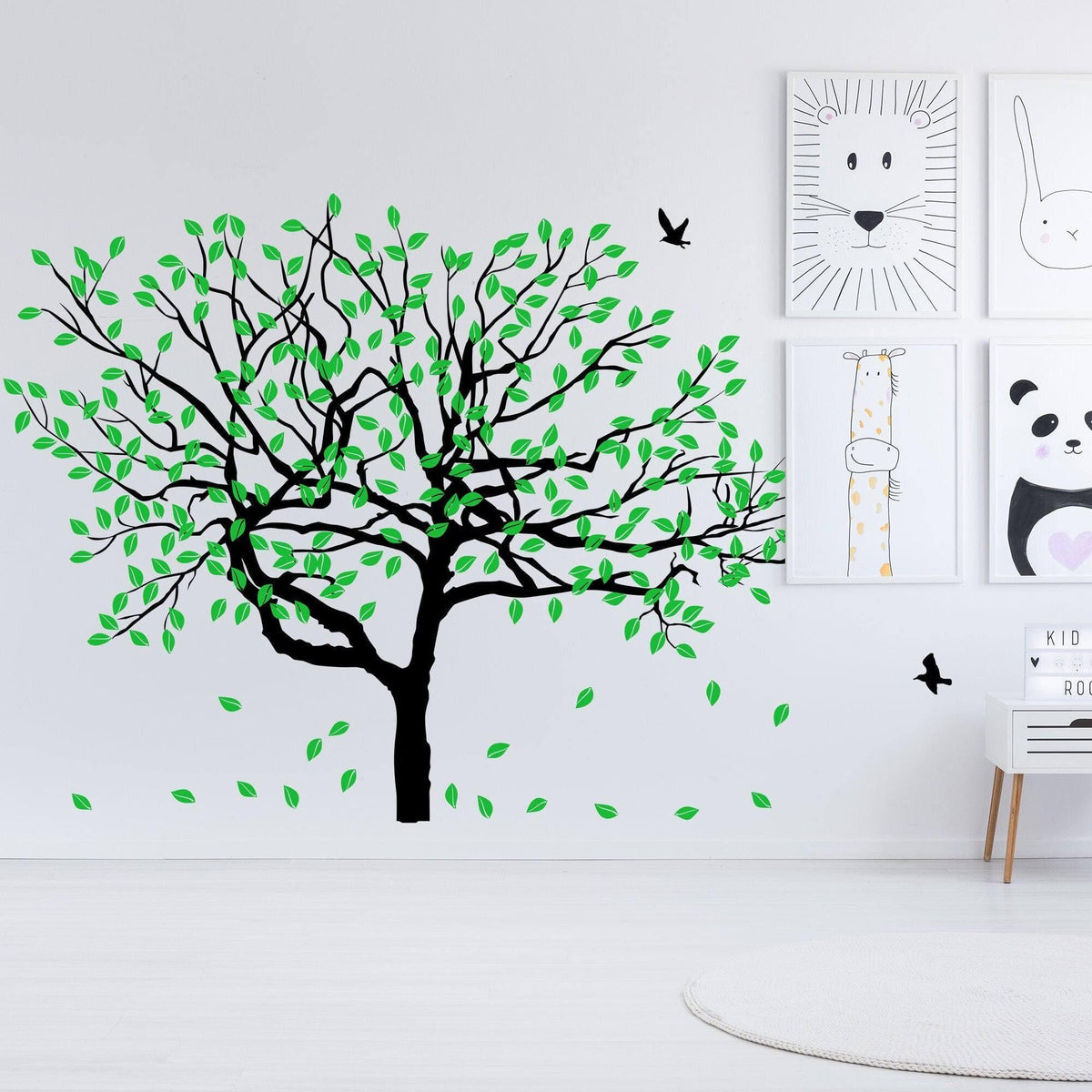 Serenity Tree Wall Sticker with green leaves on a white wall, featuring playful animal art above.