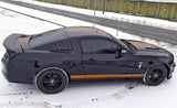 Black Mustang with orange racing stripes parked in snowy landscape showcasing stylish car decals.