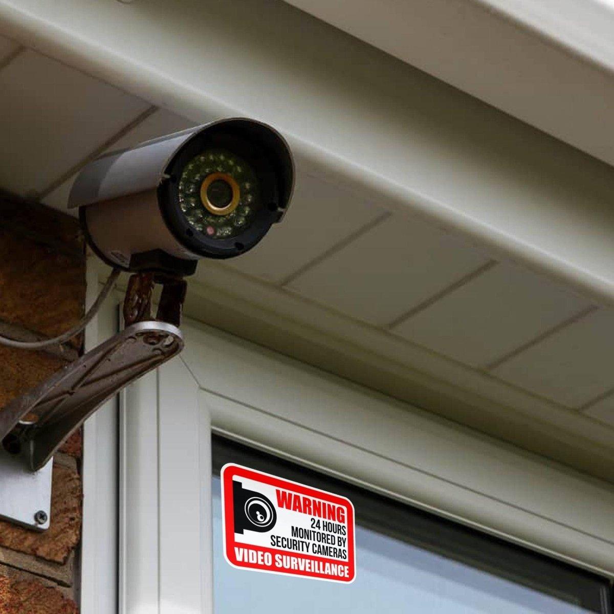 Video surveillance camera installed outside a window with a warning sign attached.