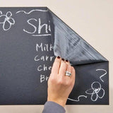Person applying a chalkboard wall sticker with chalk-written grocery list in a kitchen setting.