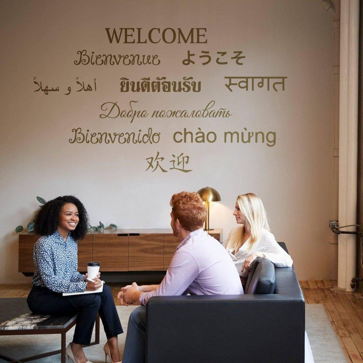 Three people chatting beneath a multilingual Welcome wall decal in a stylish interior.