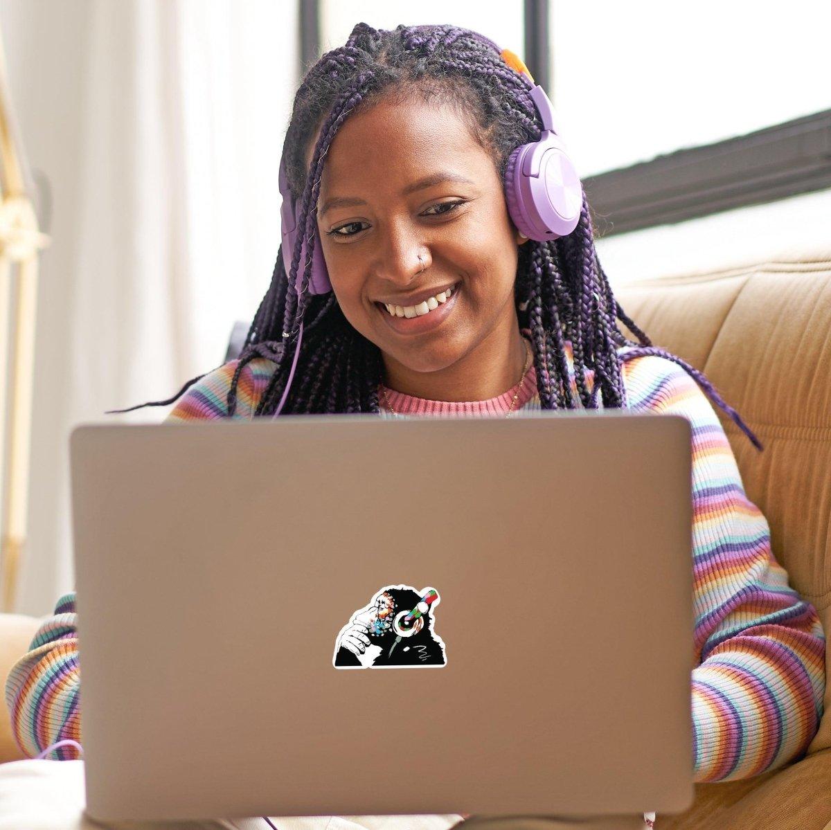Girl with braided hair enjoying her laptop featuring a playful contemplative monkey sticker.