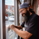 Man applying a personalized storefront window decal for a business, showcasing custom decals in action.