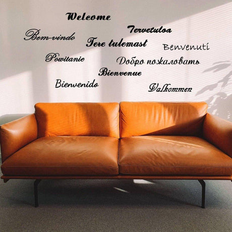Wall decal with 'Welcome' in multiple languages above a modern brown couch.