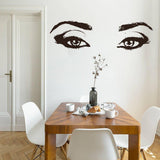 Elegant vinyl wall decal of a woman's eyes above a wooden dining table, enhancing room decor with style.