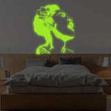 Luminous wall decal of a woman singing, glowing in green, illuminating a cozy bedroom.