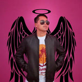 Person wearing sunglasses and a leather jacket in front of pink wall with angel wings mural.