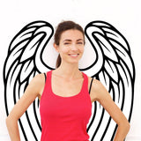 Smiling woman in red tank top with decorative angel wings wall decor behind her, showcasing bohemian style.
