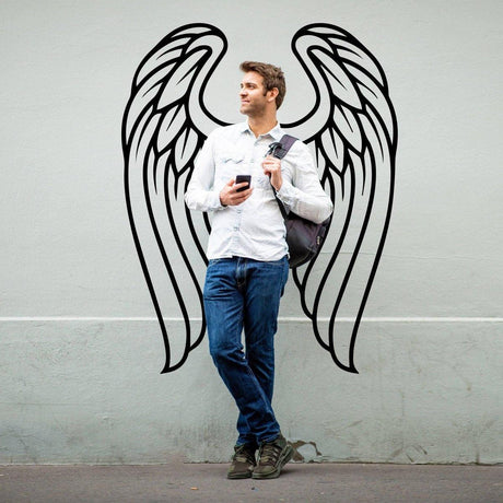 Man standing next to feathered angel wings wall decor, showcasing a stylish and bohemian wall art design.