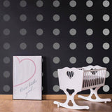 Stylish nursery featuring gray circle wall decals, a white rocking crib, and framed art on a black wall.