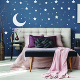 Cozy bedroom with navy wall adorned by white stars and moon wall stickers, featuring stylish bedding and decor.