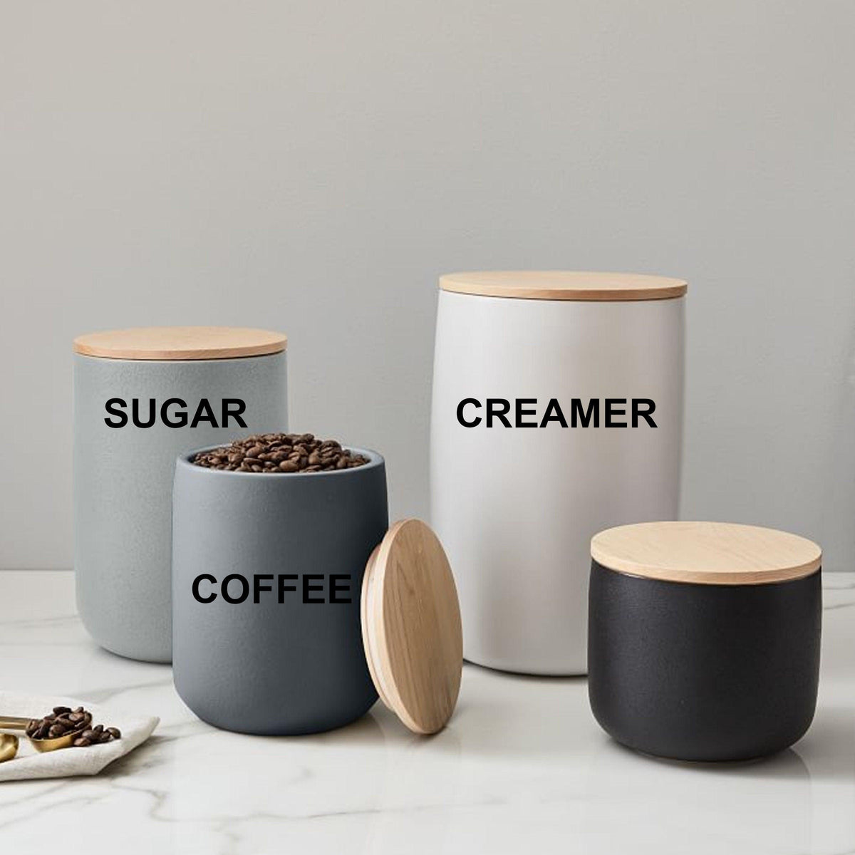 Set of stylish kitchen storage jars labeled Coffee, Sugar, and Creamer with wooden lids on a marble countertop.
