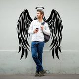 Man standing by angel wings vinyl decal, showcasing elegant wall decor for a stylish touch.