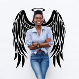 Smiling woman standing in front of black angel wings vinyl decal on white wall, showcasing whimsical wall decor.