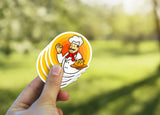 Hand holding colorful chef stickers outdoors with a blurred natural background.