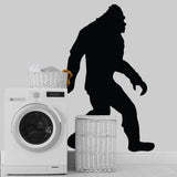 Big Foot Sasquatch vinyl wall decal on a gray wall near a washing machine and laundry baskets.