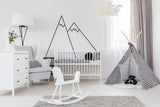Stylish nursery with black mountain wall decals, crib, rocking chair, and playful teepee decoration.