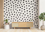 Modern black polka dots wall decal on white wall above wooden sideboard with indoor plant.
