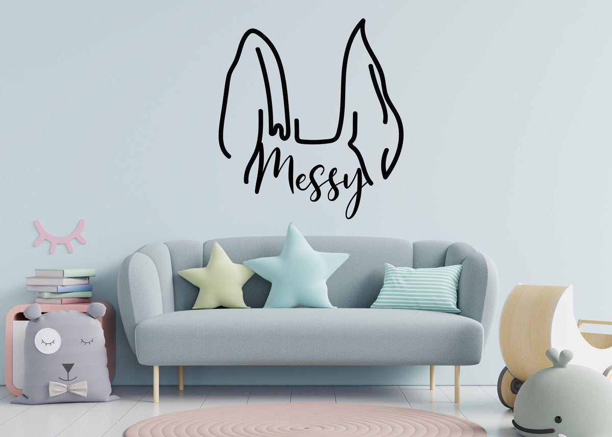 Custom pet ear wall decal with 'Messy' text above a cozy couch in a stylish room.