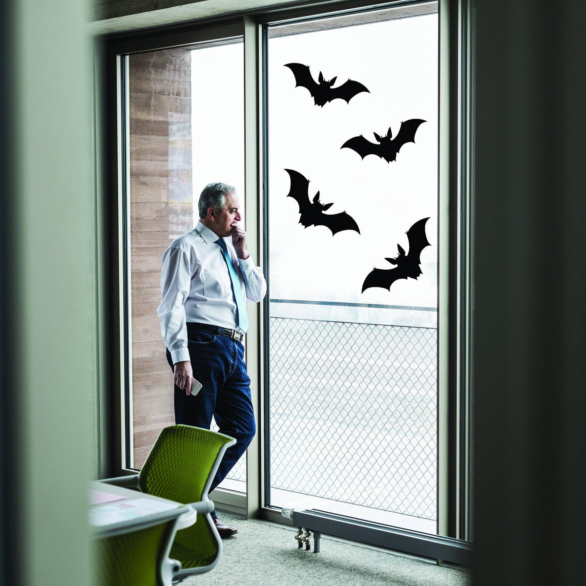 Businessman standing near Halloween bats window decals, adding spooky charm to office space for October 31st.